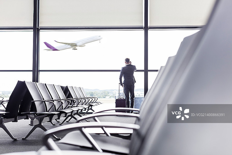 在机场出发区窗口用手机交谈的拉杆箱商人图片素材