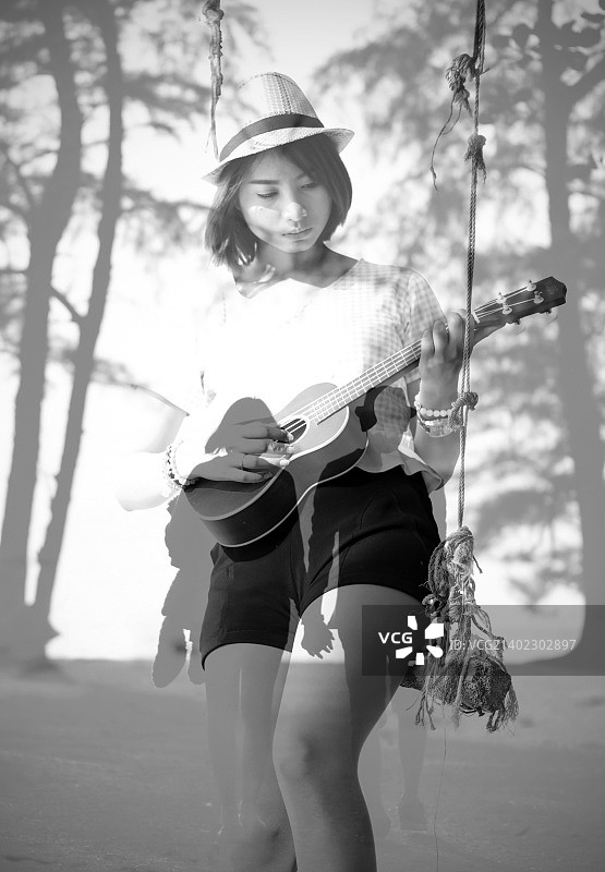 孤独的女人在海边秋千上弹尤克里里图片素材