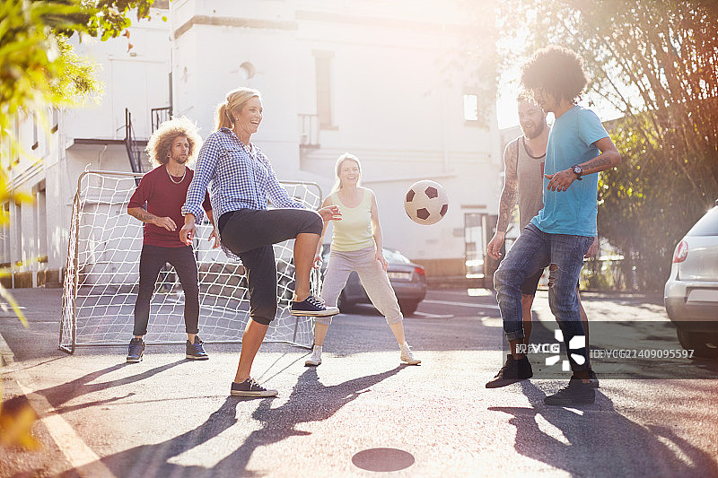 朋友们在阳光明媚的夏日街道上踢足球图片素材