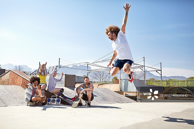 朋友们在阳光明媚的滑板公园观看并欢呼男子玩轮滑图片素材