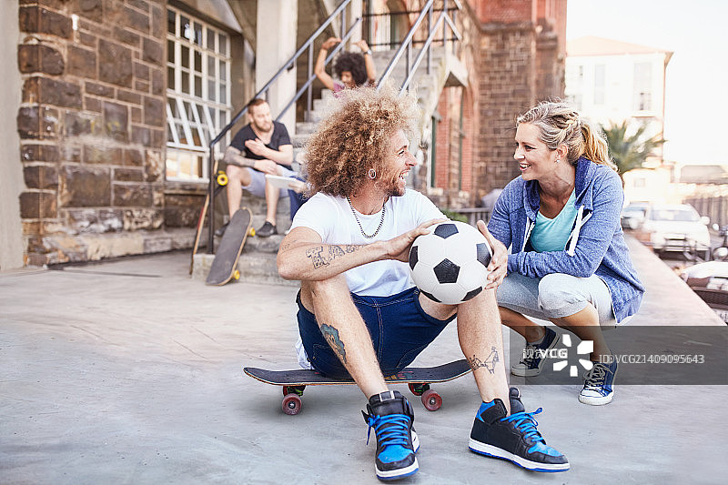 情侣在城市人行道上交谈，手拿足球和滑板图片素材