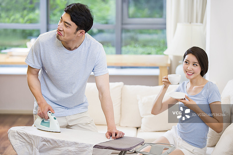 熨衣服的年轻男士和喝茶的妻子图片素材