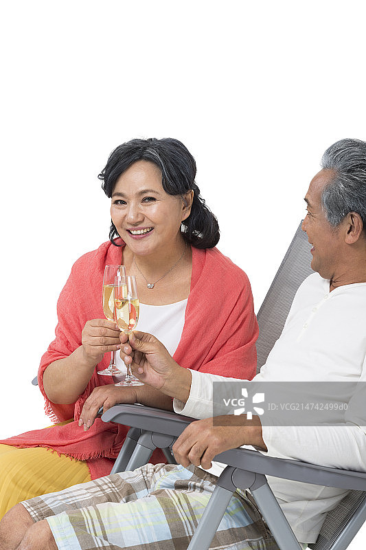 快乐的老年夫妇坐在沙滩椅上喝香槟酒图片素材