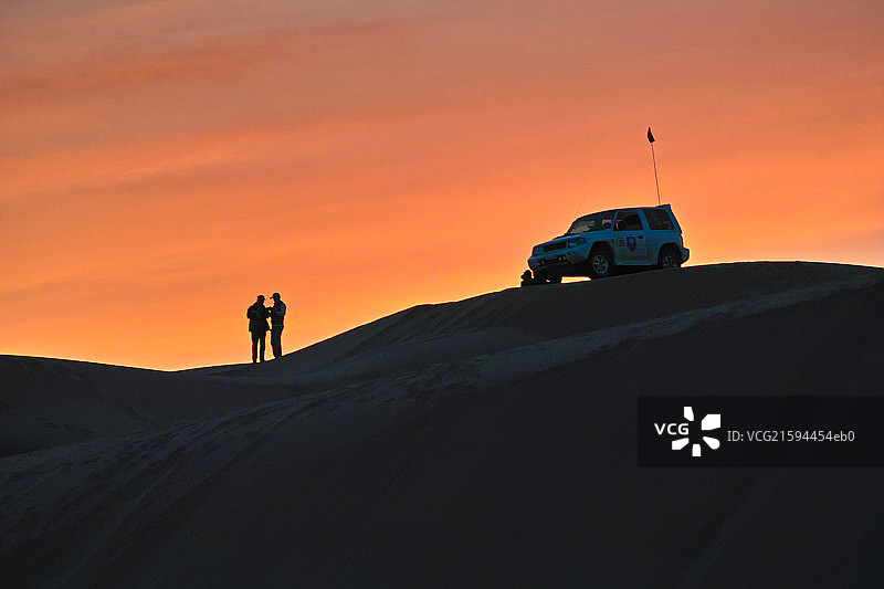 Silhouette of two persons and one SUV at sunset  on sand dune图片素材