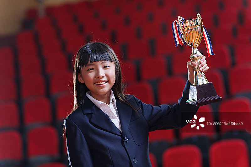 小学女生拿着奖杯在礼堂里图片素材