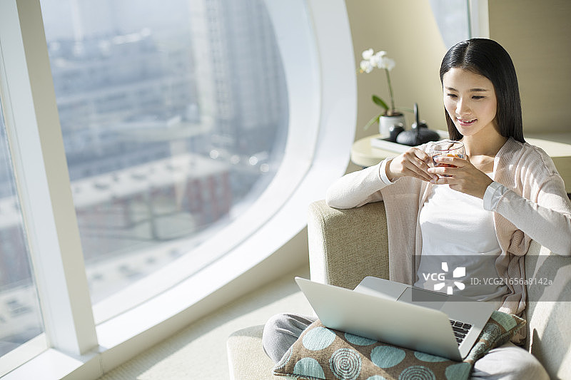 年轻女子坐在沙发上使用笔记本电脑图片素材