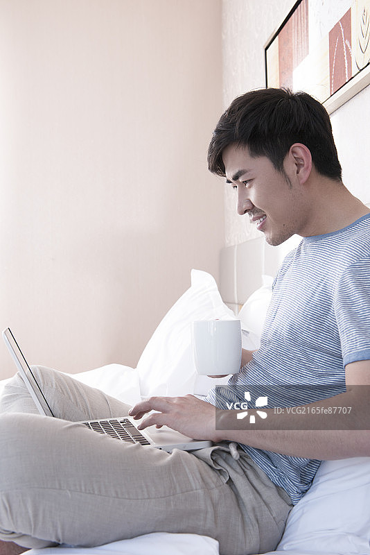 Young man using laptop in bed图片素材