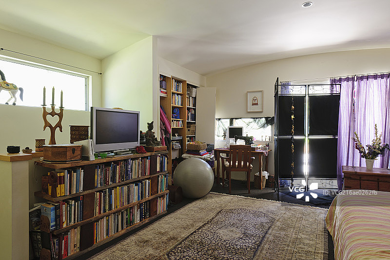 Bookshelves; study table and television with cropped bed in spacious bedroom at house图片素材