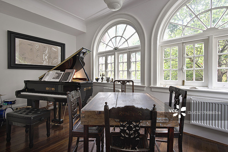 Chairs around wooden table with piano by arched French windows图片素材