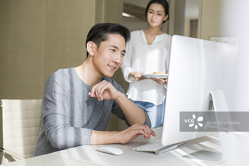 年轻女子端点心给在家工作的丈夫图片素材