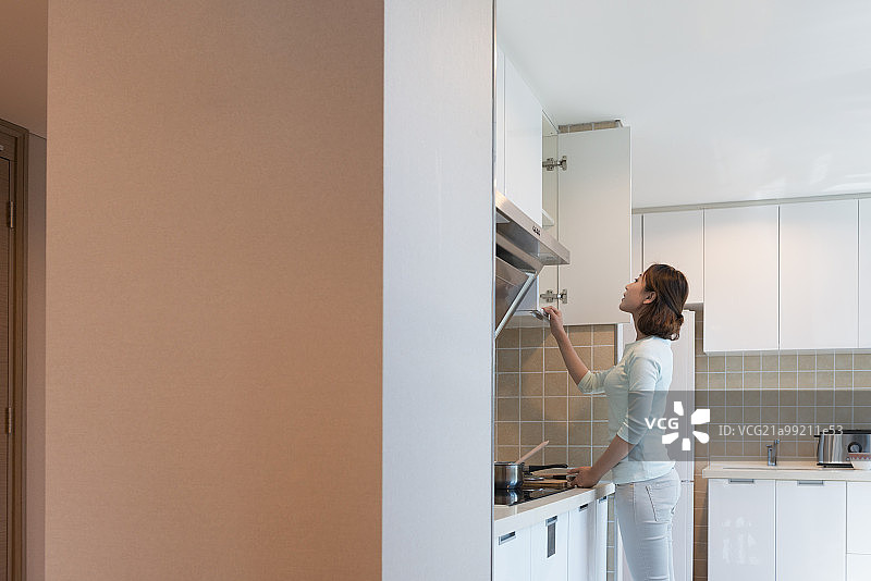 Young woman looking in cabinet in kitchen图片素材