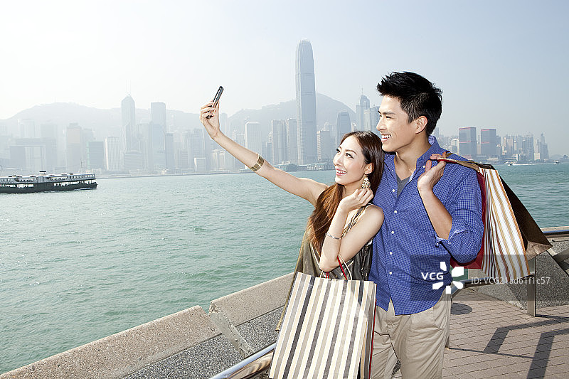 手提购物袋的年轻情侣在香港用手机自拍图片素材