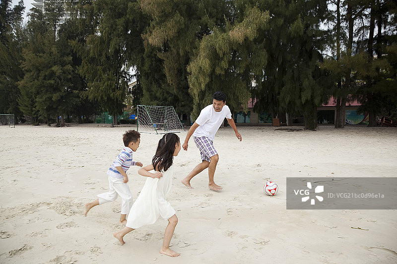 中年人和小女孩小男孩在海边踢足球图片素材