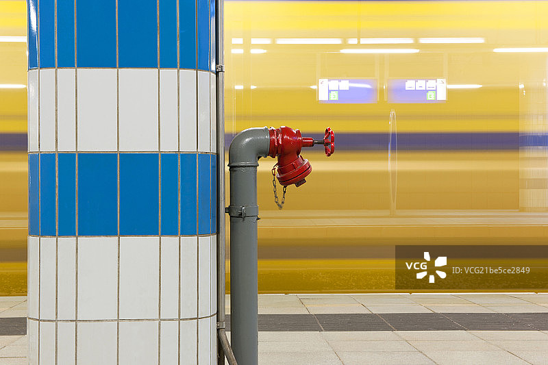 Fire hydrant on a pillar at a train station with a passing train图片素材