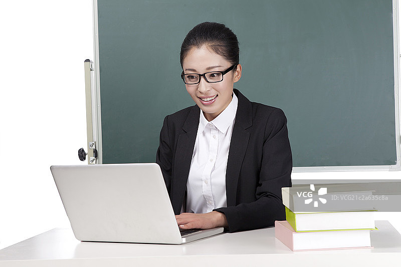 一个青年女教师坐在黑板前使用电脑备课图片素材