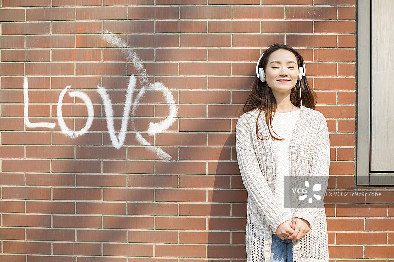 年轻女子靠着墙听音乐图片素材
