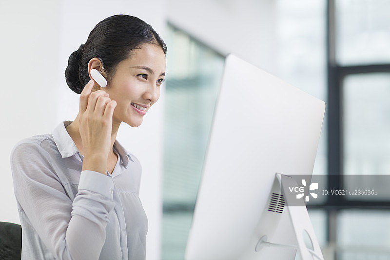 年轻商务女士戴着蓝牙耳机工作图片素材