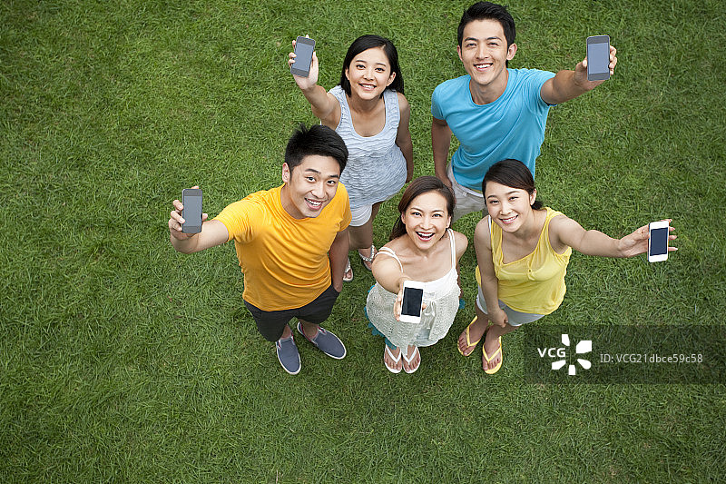 年轻男女在草地上展示手机图片素材