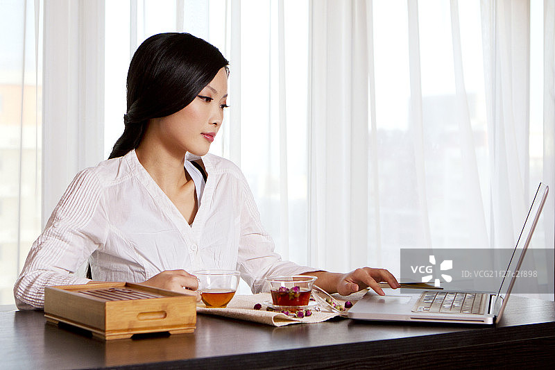 东方年轻女性喝茶和使用笔记本电脑图片素材