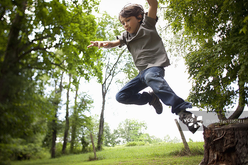 男孩从树林中的秋千绳上跳下来图片素材