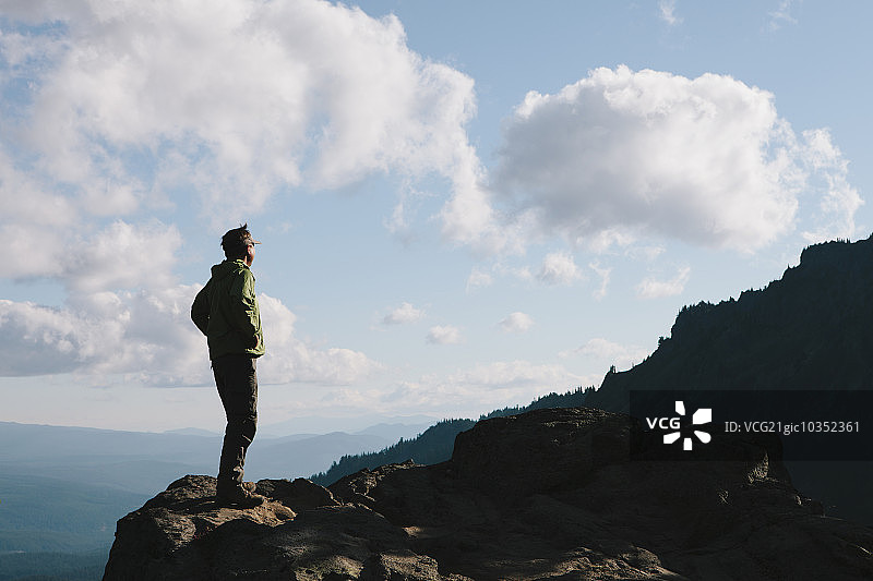 男人站在岩石峭壁上，面朝俯瞰点，黄昏时分图片素材