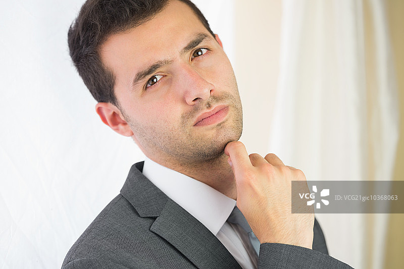 在明亮的房间里对着镜头摆姿势的英俊、不苟言笑的商人图片素材