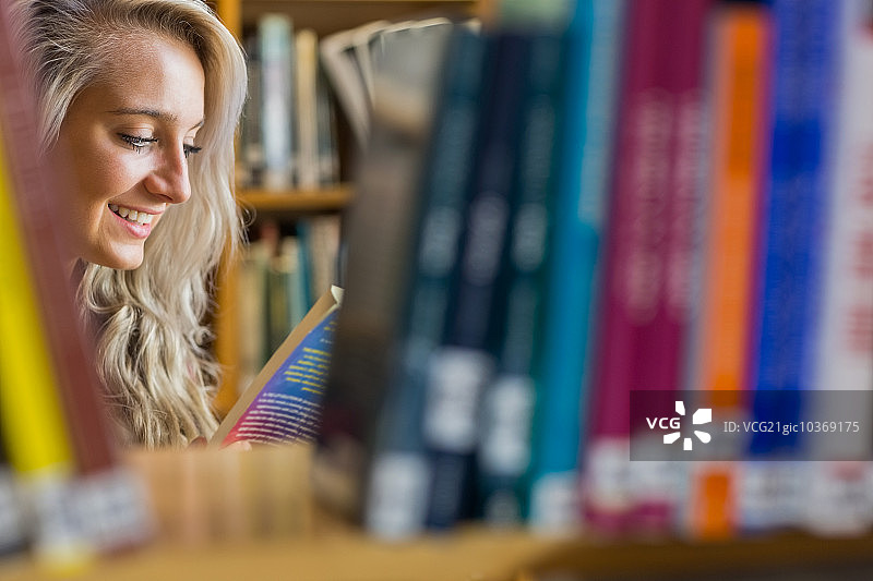 面带微笑的年轻女学生在大学图书馆书架间读书图片素材