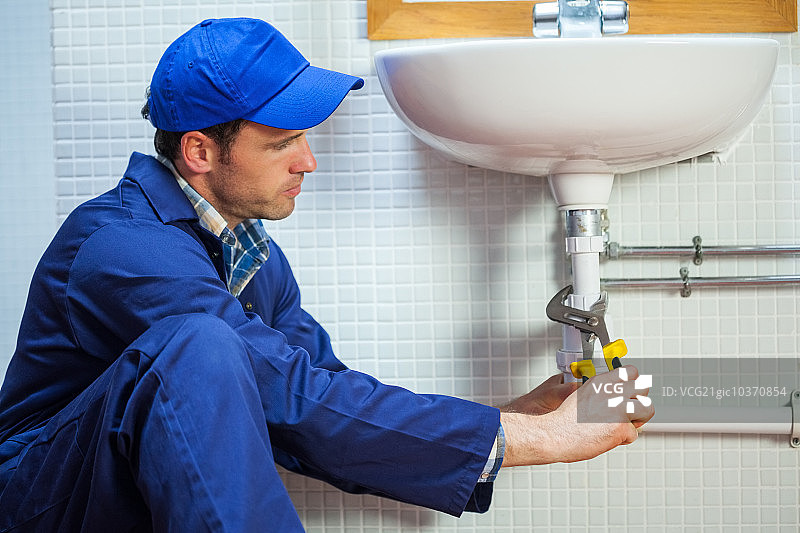在公共浴室修理水槽的专注水管工图片素材