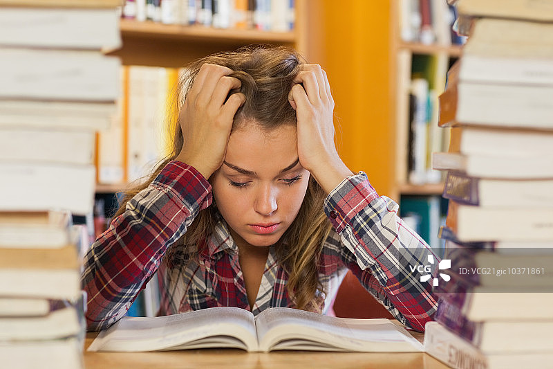 在图书馆书堆中学习的烦躁漂亮女学生图片素材