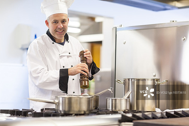 面带微笑的厨师长在专业厨房里用胡椒粉给食物调味图片素材