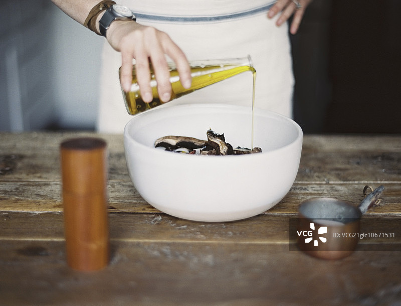 家庭厨房：一位系着围裙的女人正在碗里用油拌新鲜蔬菜沙拉图片素材