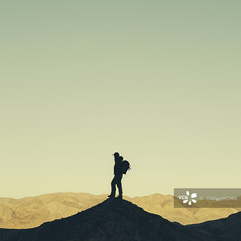 穿着背包站在死亡谷国家公园山顶上的男性徒步旅行者剪影图片素材