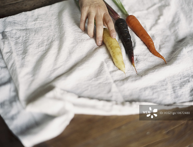 家里的餐桌：有人在白布上摆放新鲜的胡萝卜图片素材
