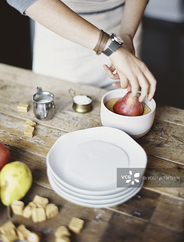 在厨房做饭的女人，将新鲜有机梨蘸入甜点酱汁，新鲜食材和红糖块图片素材