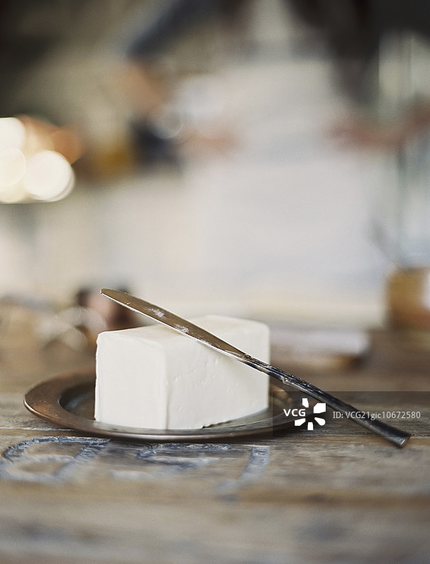 家庭厨房，背景中有一位女士，木制盘子上放着一块新鲜的有机黄油图片素材