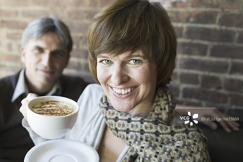 坐在咖啡店里的两人：男人和女人，手持白色瓷杯卡布奇诺咖啡图片素材