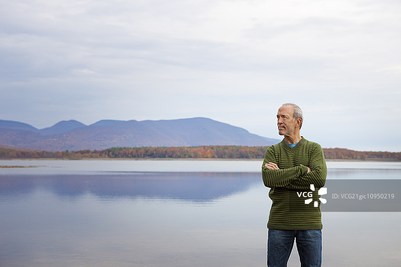 男子在平静的山间湖水旁抱臂而立图片素材