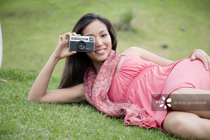 年轻女人躺在草地上用相机拍照图片素材