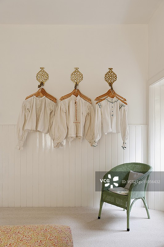 挂在白色墙上装饰的古董匈牙利亚麻罩衫和衬衫，绿色劳埃德卢姆椅子上方图片素材