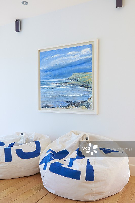 海景画下，浅色木地板上的白色和蓝色懒人沙发图片素材