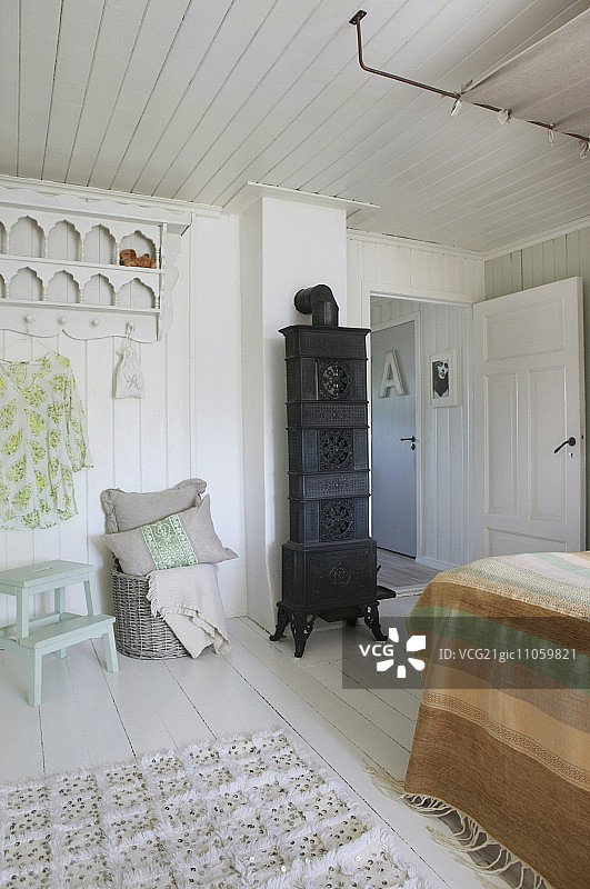 白色木墙房间内的黑色火炉、衣架和豪华床图片素材
