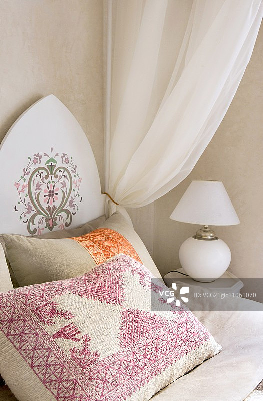 东方风格床头板刺绣靠垫与白色床幔，床头柜上的白色球形台灯图片素材