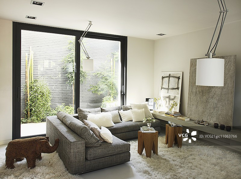 转角沙发，带小桌子和Flokati地毯，正对着可欣赏植物墙景色的滑动玻璃门，现代艺术和大象雕塑图片素材