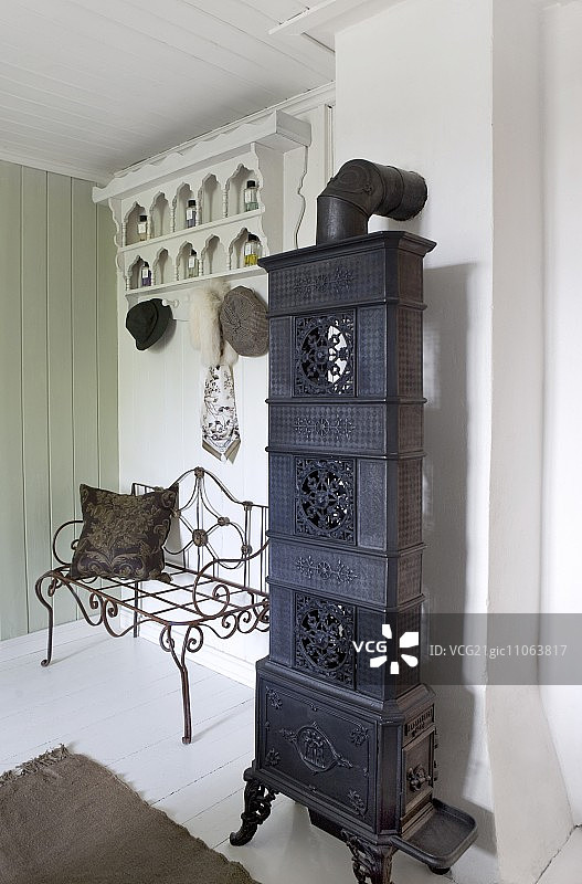 木质门厅中外套架下精致金属长凳旁的古董炉灶图片素材