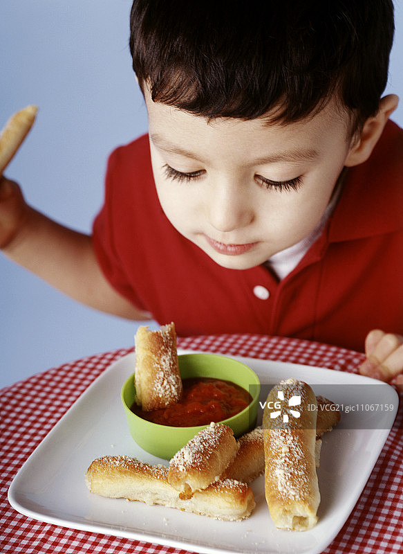 男孩将披萨面包条蘸入番茄酱碗中图片素材