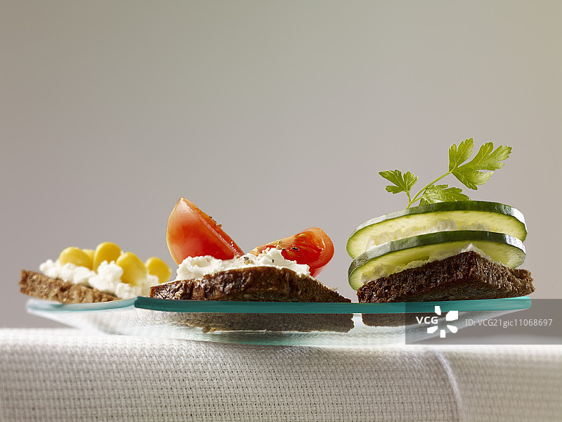 分别搭配农家奶酪、甜玉米、番茄和黄瓜的三片面包图片素材