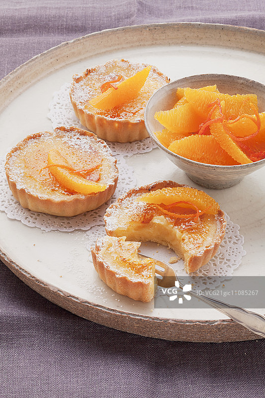 圆形托盘上的三个橙色蛋挞和橙子图片素材