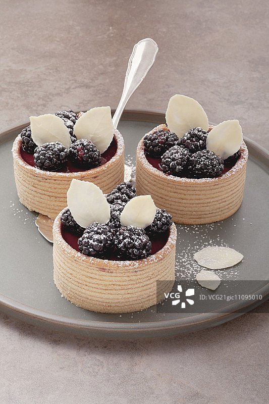 灰色盘子上配有黑莓奶油和黑莓的三份小年轮蛋糕图片素材
