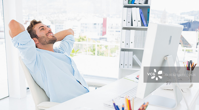 在明亮办公室里双手放在脑后休息的年轻男人图片素材