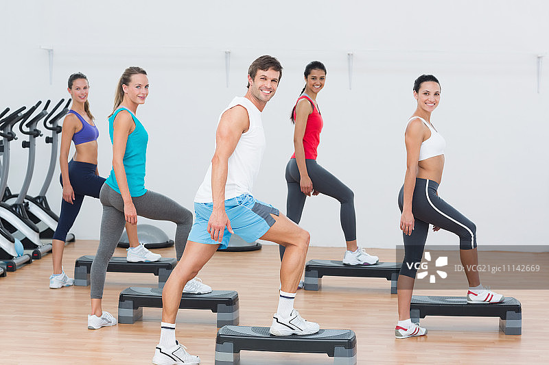 教练与健身班在健身房进行踏板健美操练习图片素材